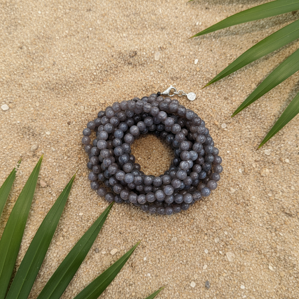 Black bone bracelet resting on warm beach sand with tropical leaves